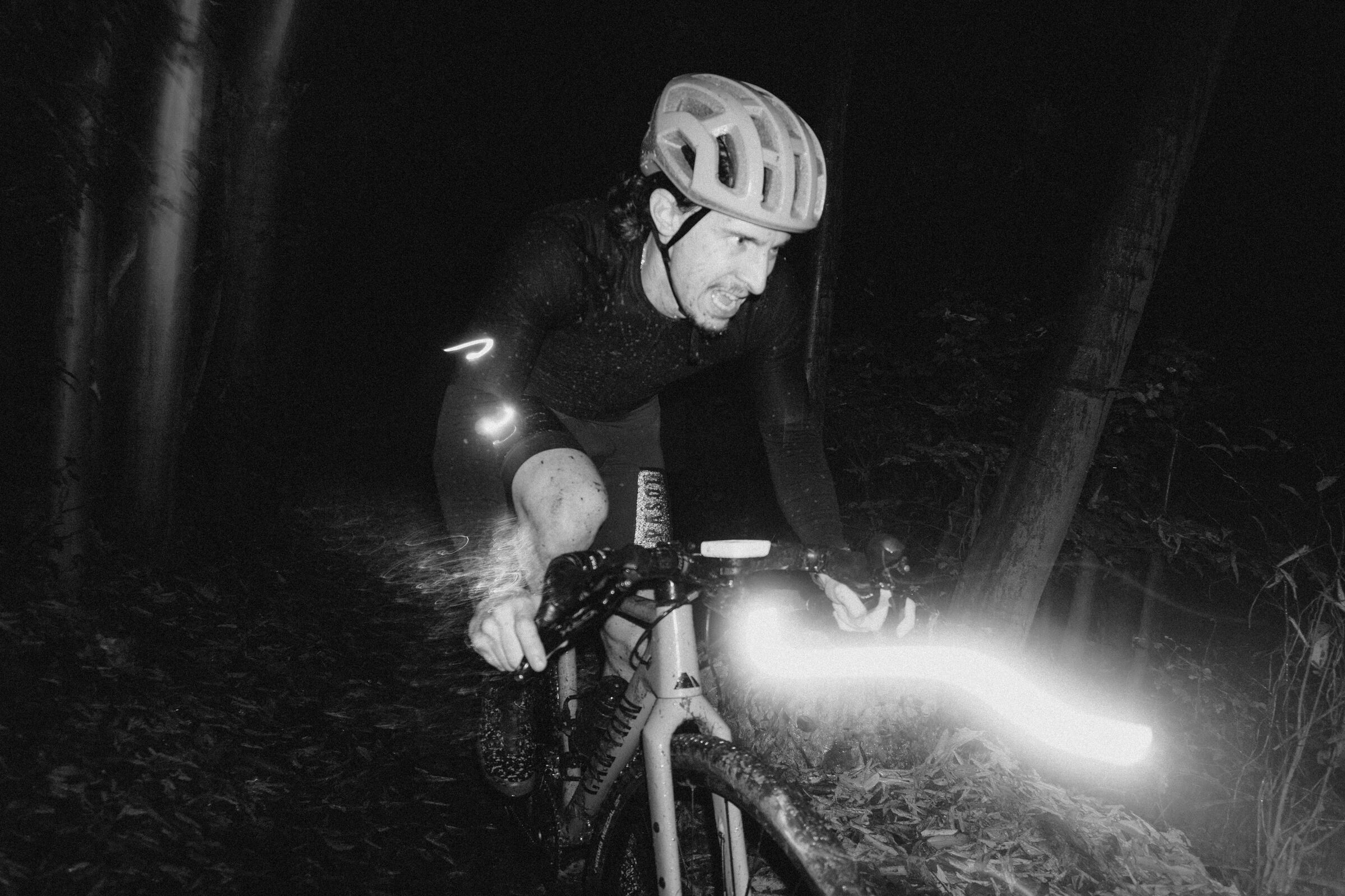 A gravel cyclist riding a forest trail at night, lit by a bike light